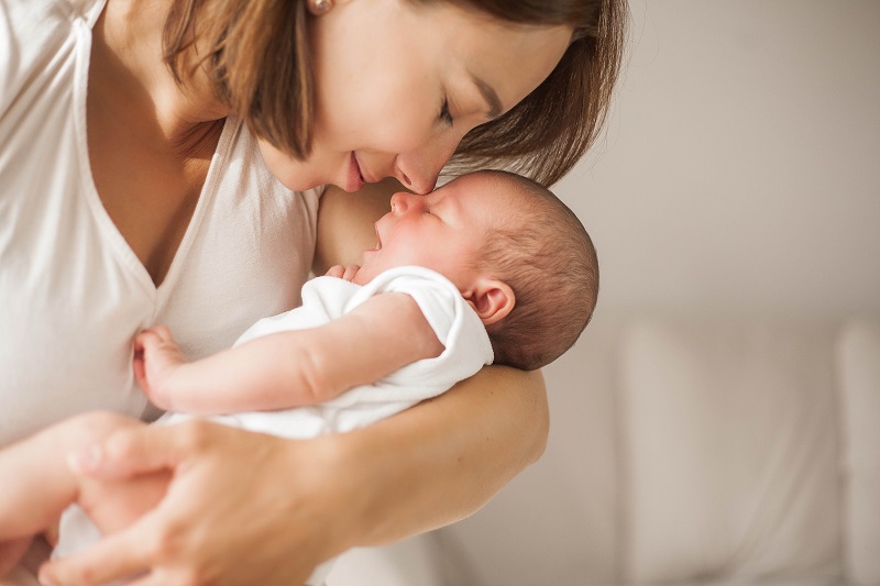 Cute newborn baby sleeping in mother’s arms. Motherhood.