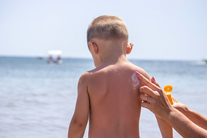 Mother puts cream on her son’s back. Caring for baby skin. Sunscreens in the travel